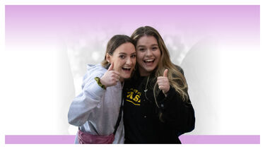 Two female students in Varsity colours giving a thumbs up