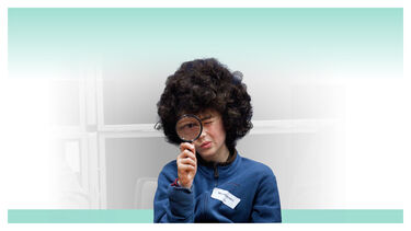 A young person looking through a magnifying glass at the camera