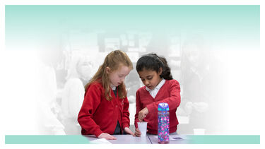 Two female primary school pupils mixing ingredients in a plastic cup