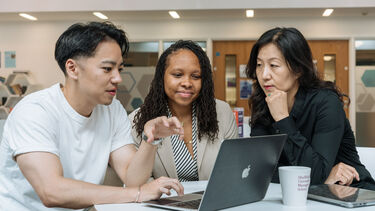 MBA students sat at a table working on a shared laptop.