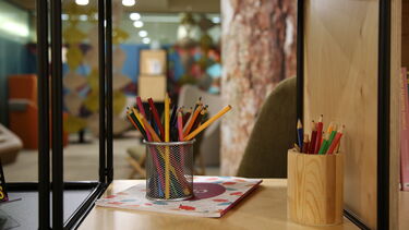 pots of crayons on a bookshelf, with the Garden Room in the background 