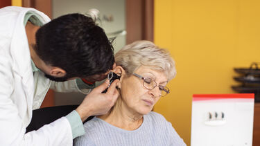 Doctor audiologist using otoscope while examining ear of his senior adult patient in doctor's office