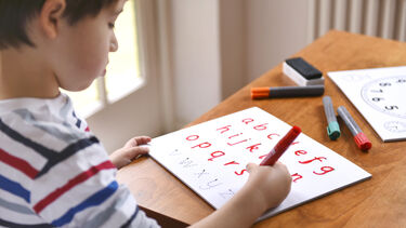 Boy is sat at a table practising his alphabet