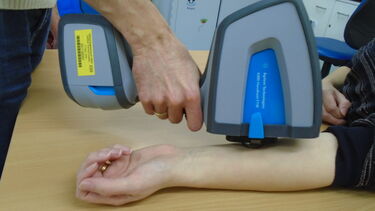 Clinician using a piece of scanning equipment on a patient's arm.