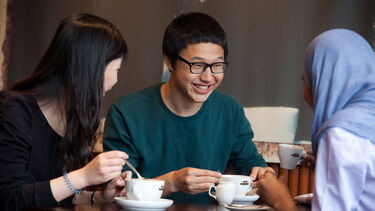 Three people sat around a table drinking from coffee cups and smiling