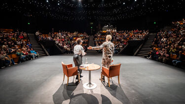 two peopel stood on a stage with audience 