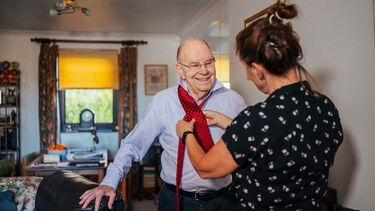 A carer helping an elderly man do up his tie