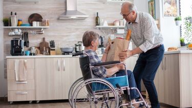 A man helping a woman in a wheelchair with her bag of shopping