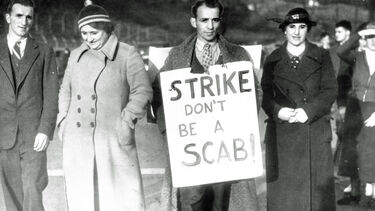 Black and white photograph of people striking, a man is holding a sign reading 'strike don't be a scab'