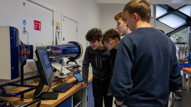 Four students stood round a computer in the fluids lab
