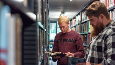 Two students reading at a book shelf in Weston library