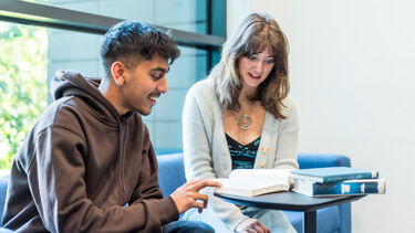Two students sat at a table smile as they discuss a book they are reading together
