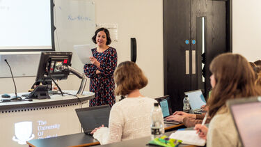 A lecturer stood at the front of a lecture theatre pointing to a passage from a book