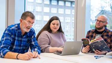 3 mature students working together using books and a laptop