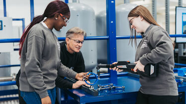 Two apprentices at the AMRC Training Centre using tools and being advised by an tutor