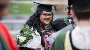 A graduate holding flowers and smiling