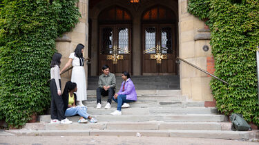 A group of five postgraduate student sitting talking on the steps of Firth Court in Sheffield