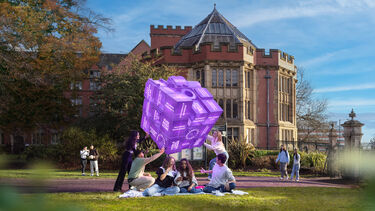 Students sitting in Weston Park looking up at a purple fortune telling cube that represents the different experiences people have at the University of Sheffield