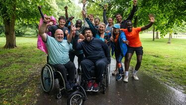 Two wheelchair users at the forefront of a group celebrating completing a race