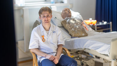 Harry, a male student nurse, sits in front of a hospital bed with an NG tube manikin.