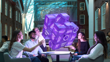 A group of students sitting in the Heartspace looking up towards a glowing purple fortune telling cube