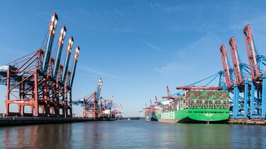 A large ship in the docks carrying large freight
