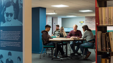 Small group of students sat working around a table in a library setting