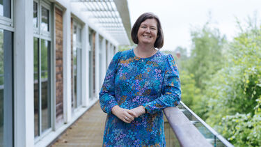 A person standing on a balcony, with windows and trees in the background.