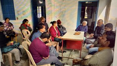 Alt text: A group of people sitting together around a table with some of them engaged in conversations and some of them smiling