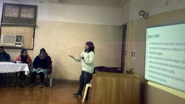 Alt text:&nbsp;A woman presenting with a projected slide on "What is PAR?" and people listening at a table. The slide has the text - What is PAR?