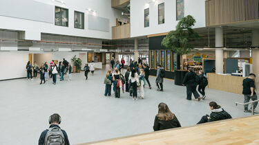 Interior shot of a large open plan building. Students walk through.