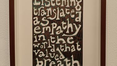 A hand-drawn text work by Jade de Montserrat. Off-white text is contrasted against a black and brown background, and reads: ‘Listening translated as empathy in the world that valued breath’.