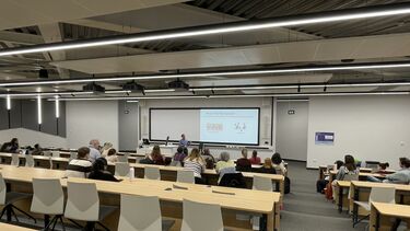 Seminar taking place in a lecture theatre. Speaker at the front of the room and students sat facing the speaker and screen.