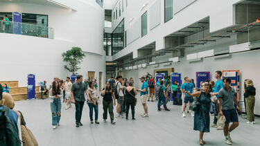 Numerous people walking around inside a bright white spacious building (The Wave). In the forefront, a person points to the left, navigating the space with the other person.