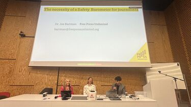 Jackie Harrison, Diana Maynard and Jos Bartmann sitting behind a table under a screen displaying the title "the necessity of a safety barometer for journalists"