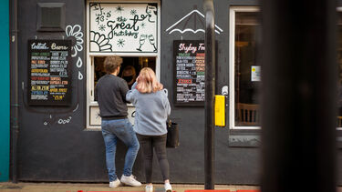 Two people ordering food at a hatch window of a food venue