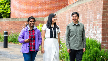 Three smiling students walk outside a red-brick building (Firth Court)