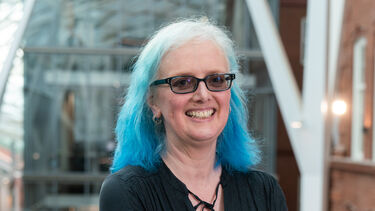 Portrait of academic with blue hair and glasses smiling