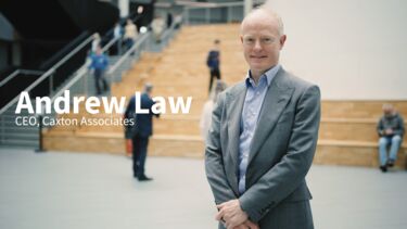 Andrew Law stands in the wave building on campus smiling at camera