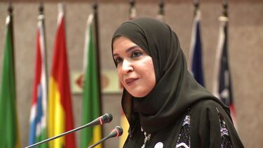Amal Al Quabaisi speaking at a dais with national flags in the background