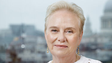 Ann Cairns smiling with a window and a cityscape in the background