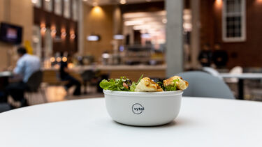 a reusable lunchbox filled with salad on a table filled 