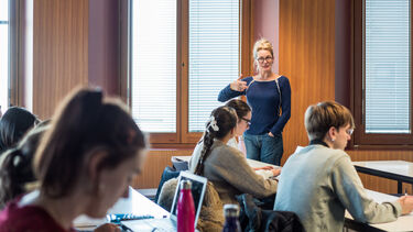 A lecturer stood in front of students, speaking and gesturing