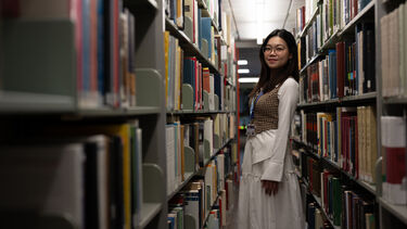 a student stood in the library between 2 bookshelves 