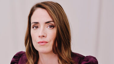 Lucy Prebble with long brown hair, pictured from the waist up in a maroon velvet dress on an orange chair