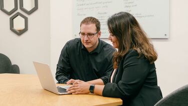 Two academics sat at a table sharing a laptop