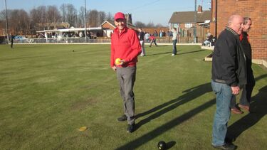 Mel Evans in a red top and peaked cap, holding a bowling ball on a green in Cradley