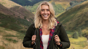 Zanna Van Dijk smiling against a backdrop of rolling hills, wearing walking gear
