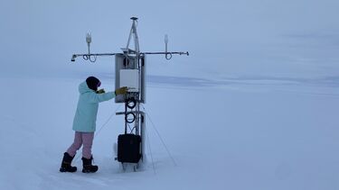 A researcher in winter clothing setting up a free standing piece of equipment in the Antarctic