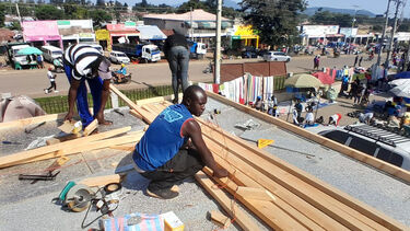 Three builders working on the roof of the sustainable cold room. They are measuring out wooden beams